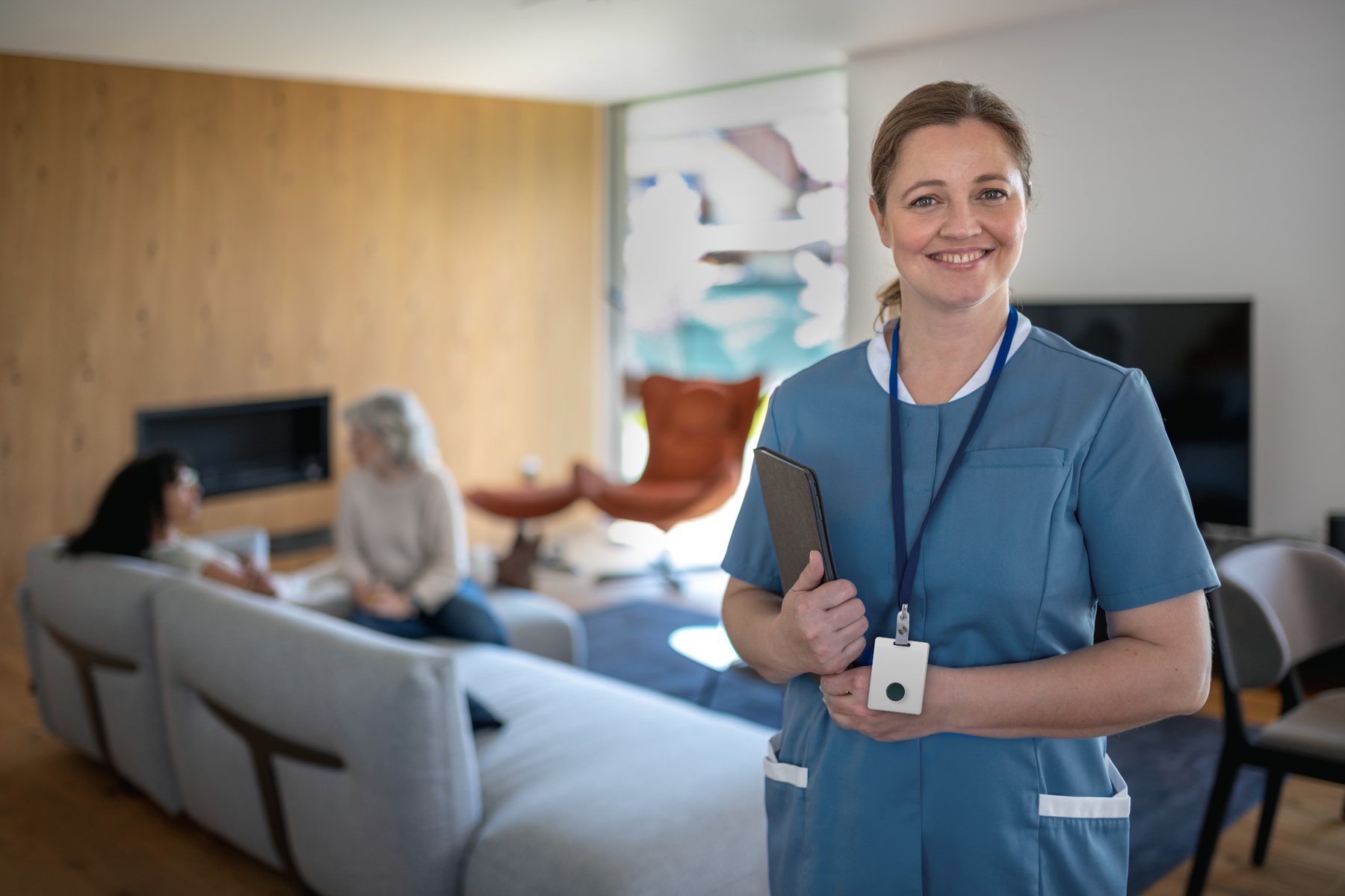 A carer in a residents' lounge, wearing the Nobi Badge on a lanyard.