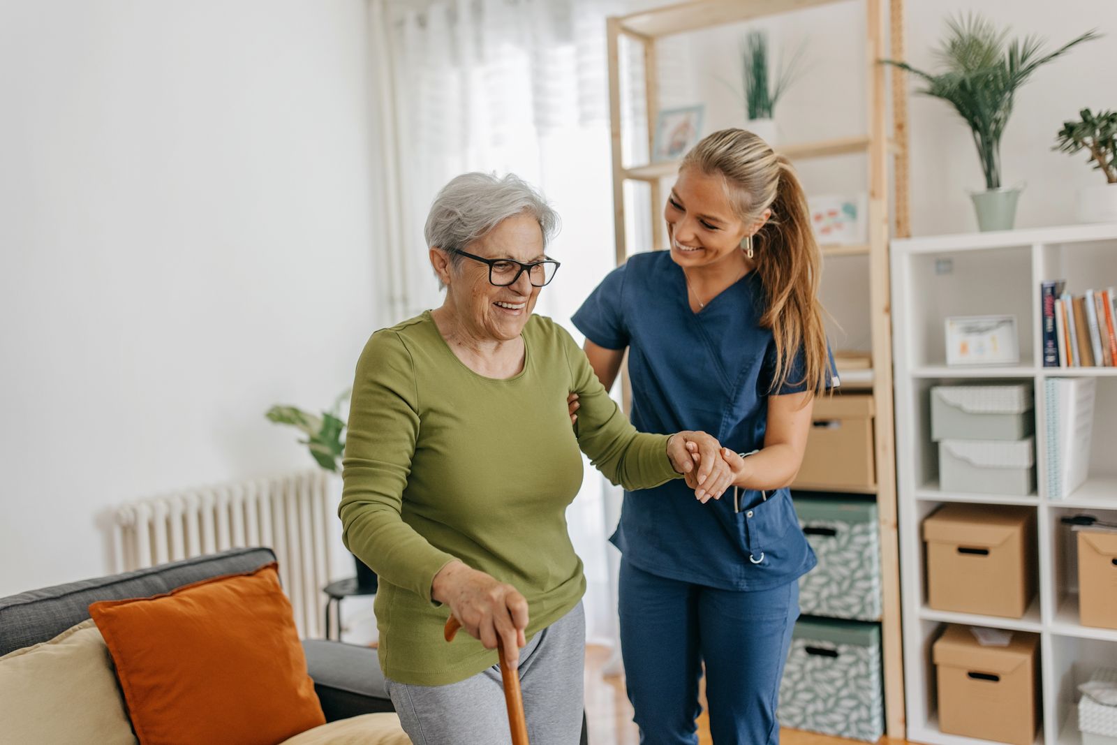 A caregiver walks with a smiling older woman who uses a cane.